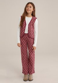 Bordeaux geklede vest en bijpassende wijde broek, met een witte langemouwen top. De outfit heeft diamanten ontwerpen en contrasterende afwerkingen.