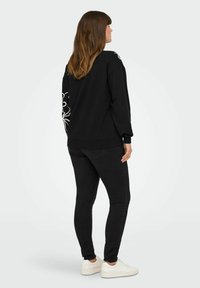 Black sweatshirt with white line art design on the left sleeve, paired with black jeans and white sneakers. Smooth fabric and relaxed fit.