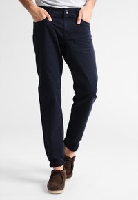 Granatowe bawełniane chinosy o slim fit, z przednimi kieszeniami, zapięciem na guzik i subtelną fakturą. Połączone z brązowymi butami w stylu mokasynów.