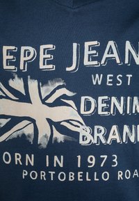 Marinblå t-shirt med en stor, urtvättad grafisk bild av den brittiska flaggan och stiliserad text i off-white. Materialet verkar mjukt och avslappnat.