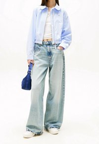 Jasnoniebieska krótka kurtka, biała koszulka na ramiączkach, oversize'owe jasnoniebieskie dżinsy z postrzępionymi końcówkami i białe trampki. Trzyma niebieską torbę na pasku.