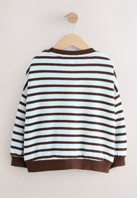 Suéter de rayas en azul claro y marrón. Presenta un cuello redondo, mangas largas y puños y dobladillo de canalé. Colgado en una percha de madera.