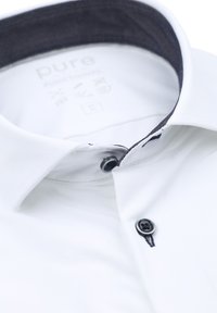 Witte katoenen shirt met een donkere kraagvoering, met een knoopsluiting en een textuurstof. Etiket zegt "puur," wat het merk aangeeft.