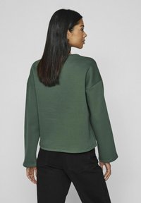 Sudadera verde de corte relajado, con cuello redondo y mangas largas. Fabricada con material suave, presenta una textura lisa y un diseño sencillo.
