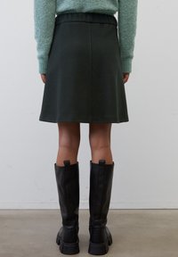 Falda acampanada de color verde oscuro con cintura elástica, combinada con botas altas de cuero negro con suelas gruesas y superficies texturizadas.