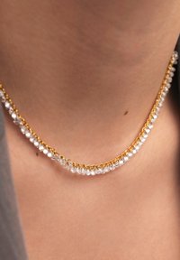Collana in oro con una fila di cristalli trasparenti. Texture liscia con superfici riflettenti. Design semplice, si appoggia sul collo.