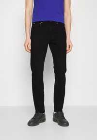 Zwarte denim jeans met een slim fit, een medium taille en een vijf-pocket ontwerp. Gepaard met een blauw T-shirt en zwarte sportschoenen.