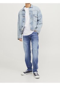 Ljusblå denimjacka med en lätt urblekt finish, vit t-shirt under, ljusblå jeans och marinblå sneakers med vita sulor.