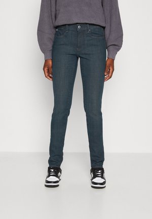 Slim-fit donkerblauwe jeans gemaakt van denim, met voorzakken, een knopenluiting en lichte vervaging op de dijen. Draag ze met zwart-witte sneakers.