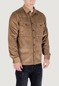 Camicia in corduroy marrone con due tasche sul petto, chiusura con bottoni e maniche lunghe. Tessuto testurizzato con righe verticali, vestibilità casual.