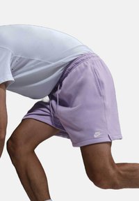Shorts Nike morados con cintura elástica y cordón, con un logo blanco en la pierna izquierda. Tejido suave, con largo hasta medio muslo.