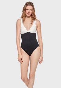 Bañador de una pieza en blanco y negro con un escote en V profundo, tirantes anchos y un diseño ajustado. La parte superior es blanca, mientras que la parte inferior es negra.