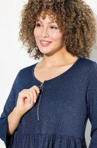 Laivastonsininen mekko teksturoidusta kankaasta, pyöreällä pääntiellä ja vetoketjuyksityiskohdalla. Mekkossa on levenevä alaosa ja kolmen neljänneksen hihat.