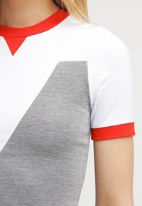 Koszulka z krótkim rękawem z czerwonym kołnierzykiem i wykończeniem, z białym korpusem i szarym geometrycznym wzorem z przodu. Gładka tekstura.