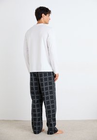 Cămașă albă cu mâneci lungi și guler rotund, asociată cu pantaloni de pijama cu carouri negre, având linii albe. Material moale, croială lejeră.