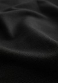 Gros plan sur un tissu noir lisse avec des plis subtils et une texture douce visible à la lumière naturelle.