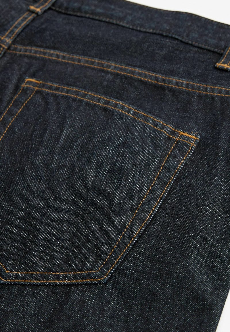 Tumedad teksad, millel on suur tagatasku oranži õmblusega, sile pind ja klassikaline viie taskuga disain.