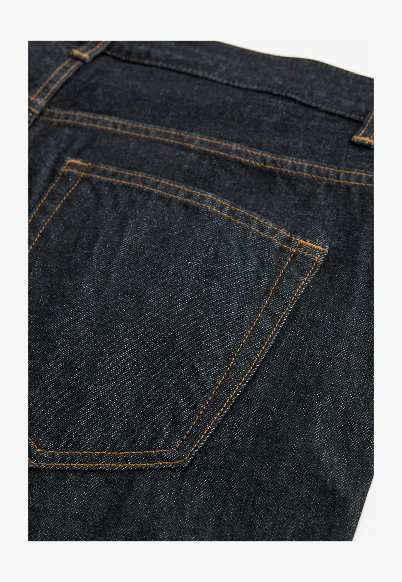 Tumedad teksad, millel on suur tagatasku oranži õmblusega, sile pind ja klassikaline viie taskuga disain.