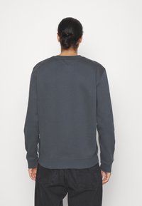 Sudadera gris oscuro con puños y dobladillo acanalados, con un cuello redondo y una textura suave y lisa, combinada con pantalones negros.
