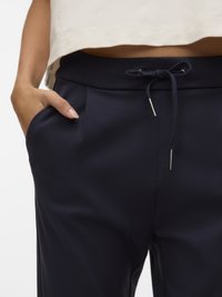 Pantaloni jogger de culoare bleumarin cu talie cu șnur, buzunare laterale și pliuri subtile, confecționați dintr-un material moale.