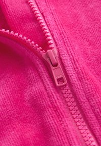 Mikroplyšová látka v jasně růžové barvě s hladkou texturou, s růžovým zipem podél jednoho okraje. Zuby zipu jsou malé a těsně vedle sebe.