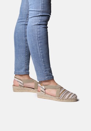 Striped espadrille wedge sandals with a natural jute sole, beige straps, and an open heel, paired with fitted blue jeans.