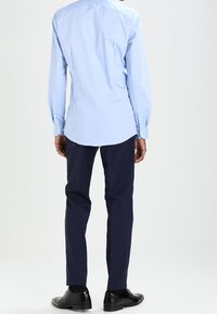 Lichtblauw overhemd met lange mouwen, gebogen onderkant, gecombineerd met donker marineblauwe broek en zwarte schoenen. Duidelijk ontwerp en getailleerde vorm.