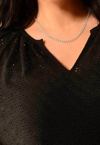 Top nero a maniche corte con un motivo floreale testurizzato e scollo a V. Presenta una collana in argento con link intrecciati.