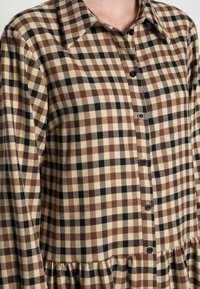 Robes chemises à carreaux marron et beige avec un col, des boutons à l'avant et un ourlet de jupe froncé. Fabriquée en tissu doux avec une finition texturée.