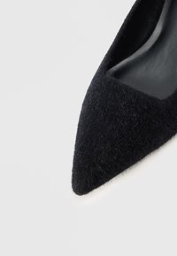 Čierne lodičky s ostrou špičkou vyrobené z mäkkého, huňatého materiálu s hladkým vnútorným podšívom. Elegantný silueta s textúrovaným povrchom a jemným leskom.
