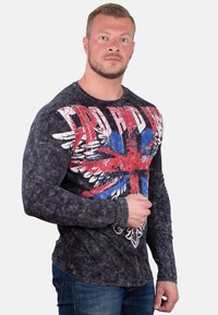 Langärmliges, schwarzes Shirt mit einer verblichenen Textur, das ein farbenfrohes Union-Jack-Design und weiße, abgenutzte Buchstaben über der Brust zeigt.
