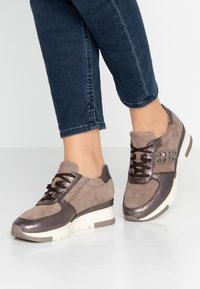 Bruna mocka och metalliska sneakers med texturerade detaljer, snörningsdesign och en något upphöjd vit sula. Har nitar på sidan.