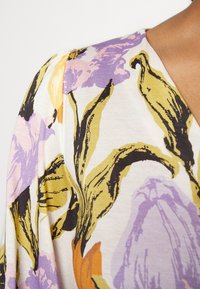 Blumendesign auf weichem, leichtem Stoff in lila, gelben und schwarzen Farbtönen. Mit einem V-Ausschnitt und leicht gepufftem Schulterdetail.