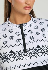 Top zip-up a fantasia bianca e nera con colletto alto, motivi a stella e una texture di tessuto liscia e elastica.