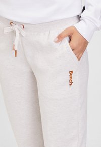 Lichtgrijze joggerbroeken met zijzakken, een tailleband met trekkoord en een oranje "Bench." logo geborduurd aan de zijkant. Zachte stof en een ontspannen pasvorm.