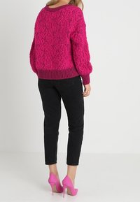 Flauschiger, hellrosa Pullover mit lockerer Passform und geripptem Kragen, kombiniert mit schwarzen Slim Jeans und rosa High Heels.