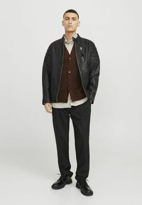 Svart läderbomberjacka med texturerade axlar, brun stickad cardigan, randig skjorta, svarta byxor och svarta snörskor.