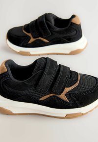 Czarno-brązowe sneakersy charakteryzują się połączeniem siateczki i zamszu, mają dwa paski na rzepy oraz białą podeszwę środkową. Gumowa podeszwa zewnętrzna zapewnia przyczepność.
