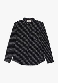 Chemise noire à manches longues avec un motif de texte blanc répété indiquant "SCOTCH & SODA." Design à col avec un ourlet arrondi.