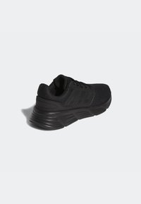 Zapatilla deportiva negra con parte superior de malla, tejido texturizado, talón reforzado y suela de goma, con un sutil logotipo en los laterales.