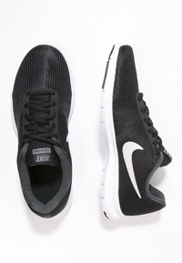 Pár černých tréninkových bot Nike Flex Bijoux s bílými podrážkami a bílým logem Nike, zobrazených z pohledu shora a z boku na bílém pozadí.