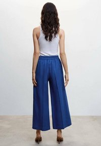 Blauwe wijde broek met een gladde, lichte stof. Voorzien van een elastische tailleband en een ontspannen pasvorm met plooien voor extra designdetails.