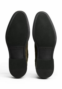 Un par de zapatos de vestir negros con suela de goma y un patrón de agarre texturizado, con la marca "Tommy Hilfiger" visible en cada suela.