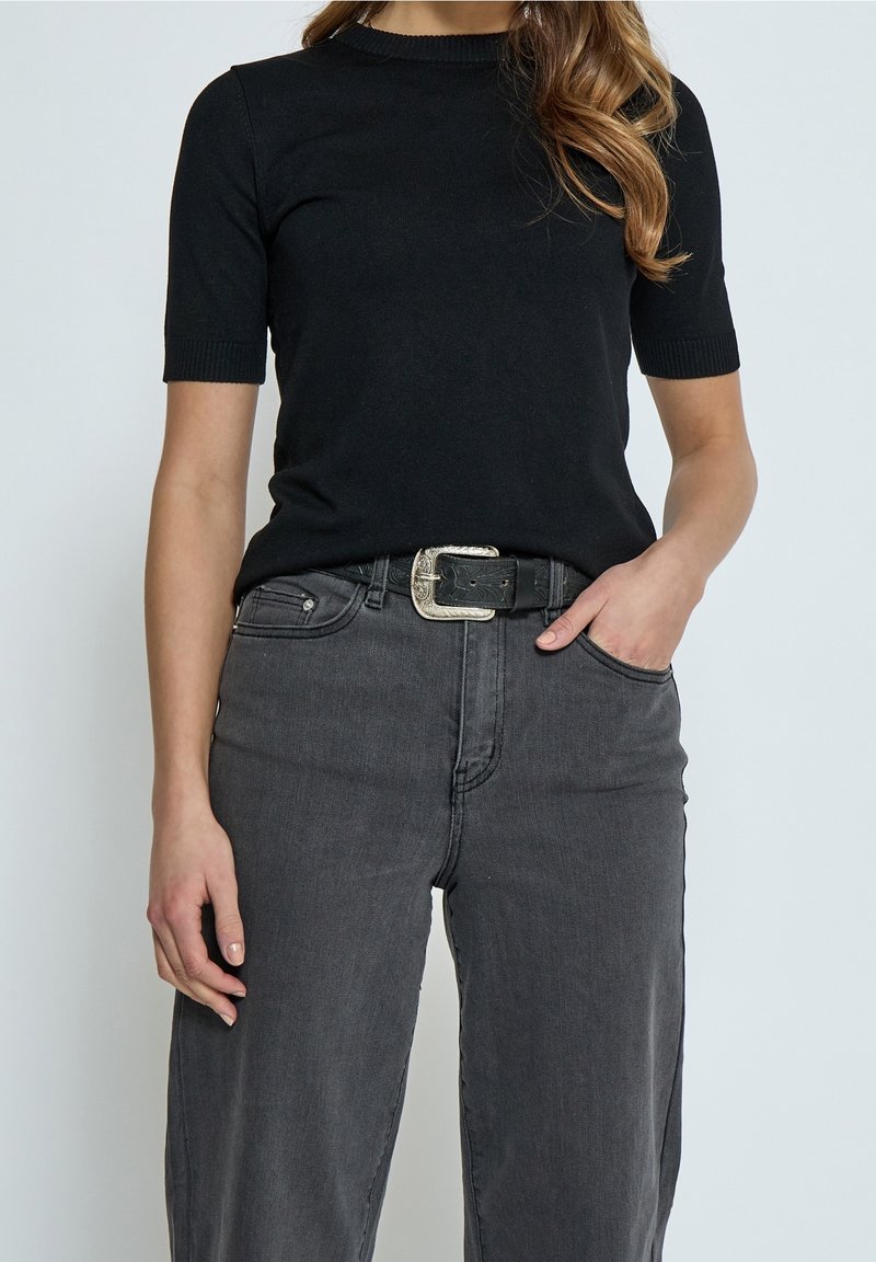 Top noir à manches courtes en tricot avec un col rond, associé à un jean en denim gris taille haute et une ceinture noire avec une boucle argentée.