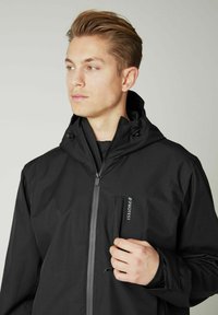 Schwarze Außenjacke mit Kapuze, Reißverschluss auf der Vorderseite und Brusttasche. Mit glattem Stoff, strukturierten Akzenten und verstellbaren Kordeln.
