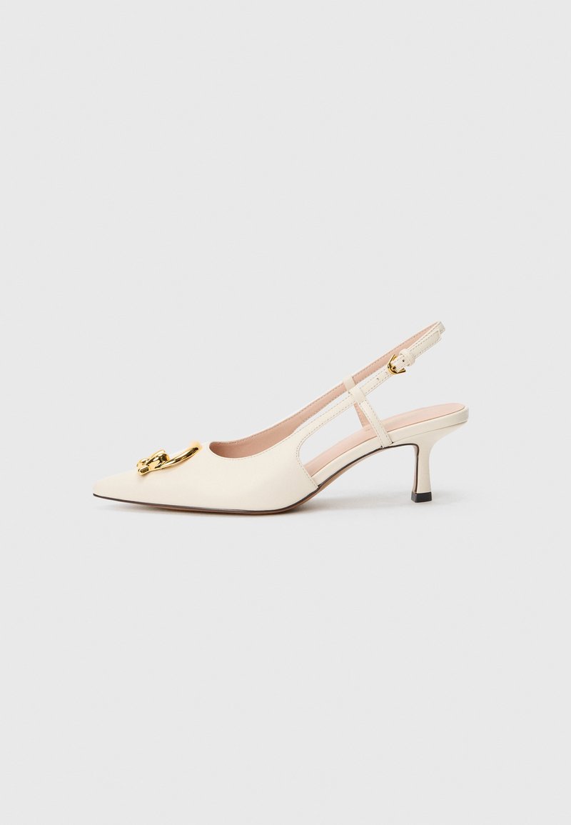 Beige slingback heels with a pointed toe, featuring a gold decorative chain, a low block heel, and cut-out side details. Smooth leather texture.