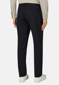 Dunkelblaue Hosen aus glattem Stoff, mit Gesäßtaschen und einer taillierten Passform. Kombiniert mit weißen Sneakers für einen Kontrast.