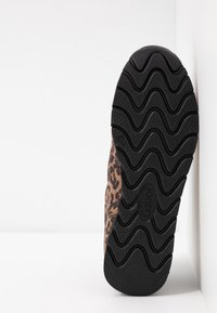 Semelle d'une chaussure à imprimé léopard inclinée vers le haut, montrant une semelle en caoutchouc noire ondulée avec le nom de la marque "Gabor" embossé au centre.