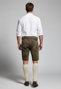 Herren Shorts aus braunem Leder mit strukturierter Oberfläche, kombiniert mit kniehohen, gestrickten cremefarbenen Socken und braunen Schuhen, getragen zu einem weißen Hemd.