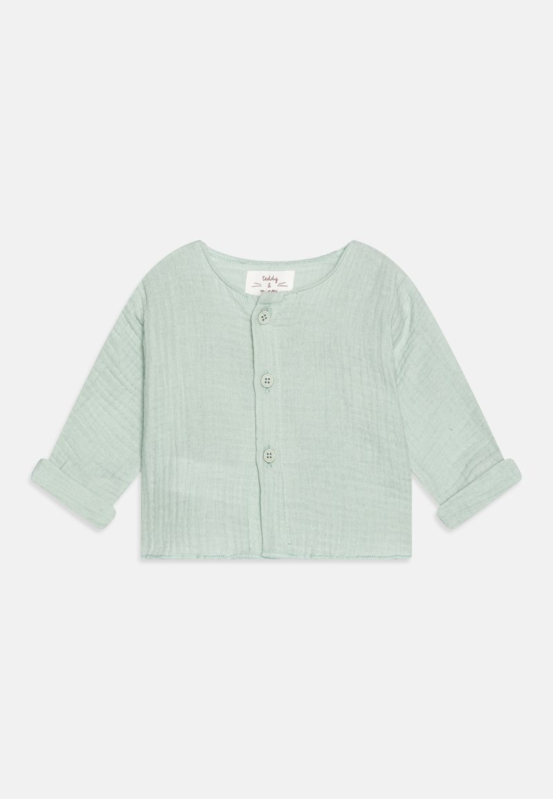 Chemise courte verte clair à col boutonné, fabriquée en tissu texturé. Elle présente un col rond et des manches roulées, avec trois boutons à l'avant.
